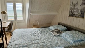 A bedroom with a bed, a desk, and a chair. There is a window with a view of the sea. - Studio Avec vue Mer, Centre de Langrune (Langrune-sur-Mer)