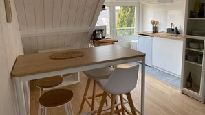 A modern kitchen with a wooden table, bar stools, and a built-in shelf with dishes. - Studio Avec vue Mer, Centre de Langrune (Langrune-sur-Mer)