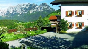 A white building with wooden shutters and a balcony, set against a backdrop of snow-capped mountains and lush green hills. - Ferienwohnung Hochkalter, Dusche/wc, 57 qm, TV, Balkon, Obergeschoss (Ramsau bei Berchtesgaden)