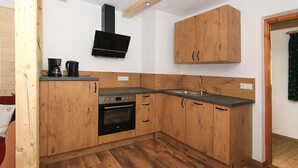 A compact kitchen with wooden cabinets, a built-in oven, a sink, and a flat-screen TV mounted above the stove. - Ferienwohnung Hochkalter, Dusche/wc, 57 qm, TV, Balkon, Obergeschoss (Ramsau bei Berchtesgaden)