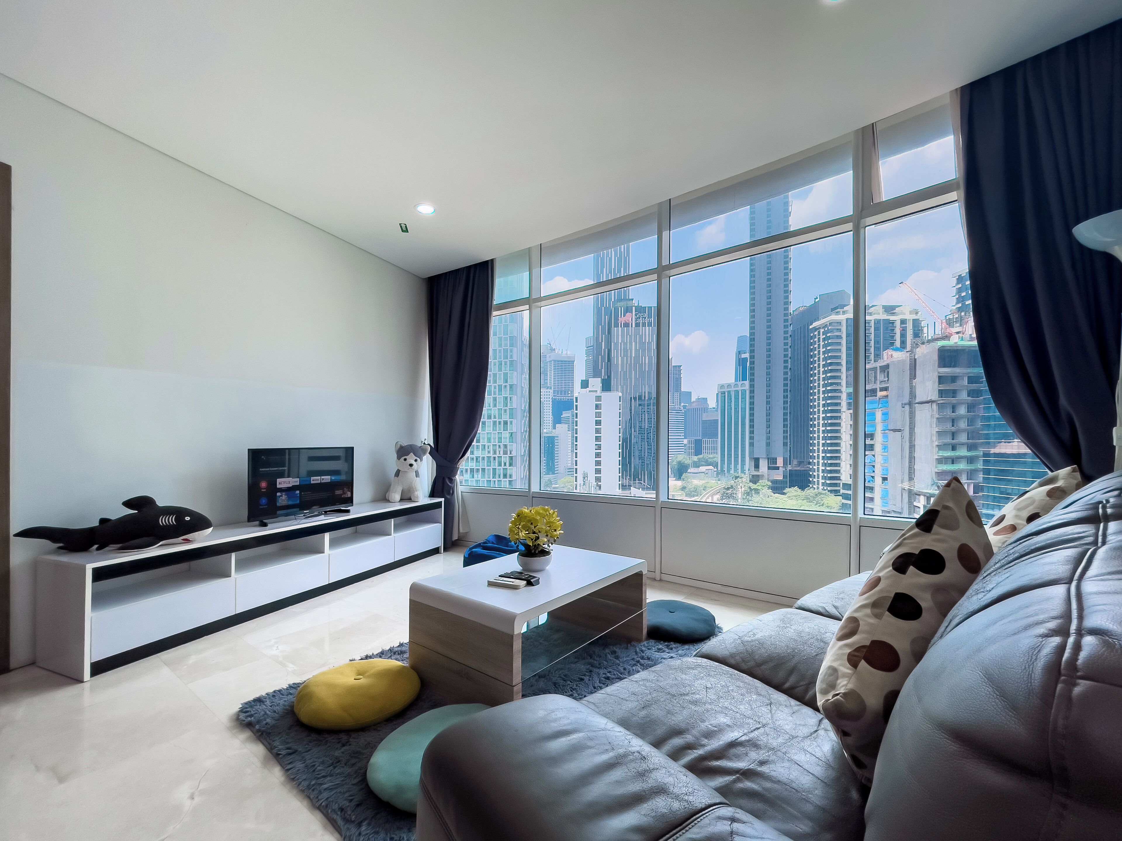 A modern living room with a sofa, a coffee table, a TV, and a city view through large windows.