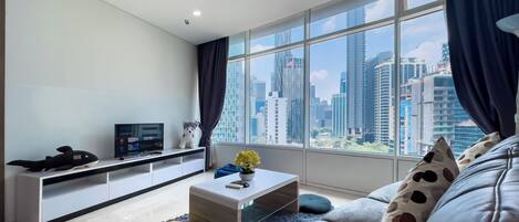 A modern living room with a sofa, a coffee table, a TV, and a city view through large windows.