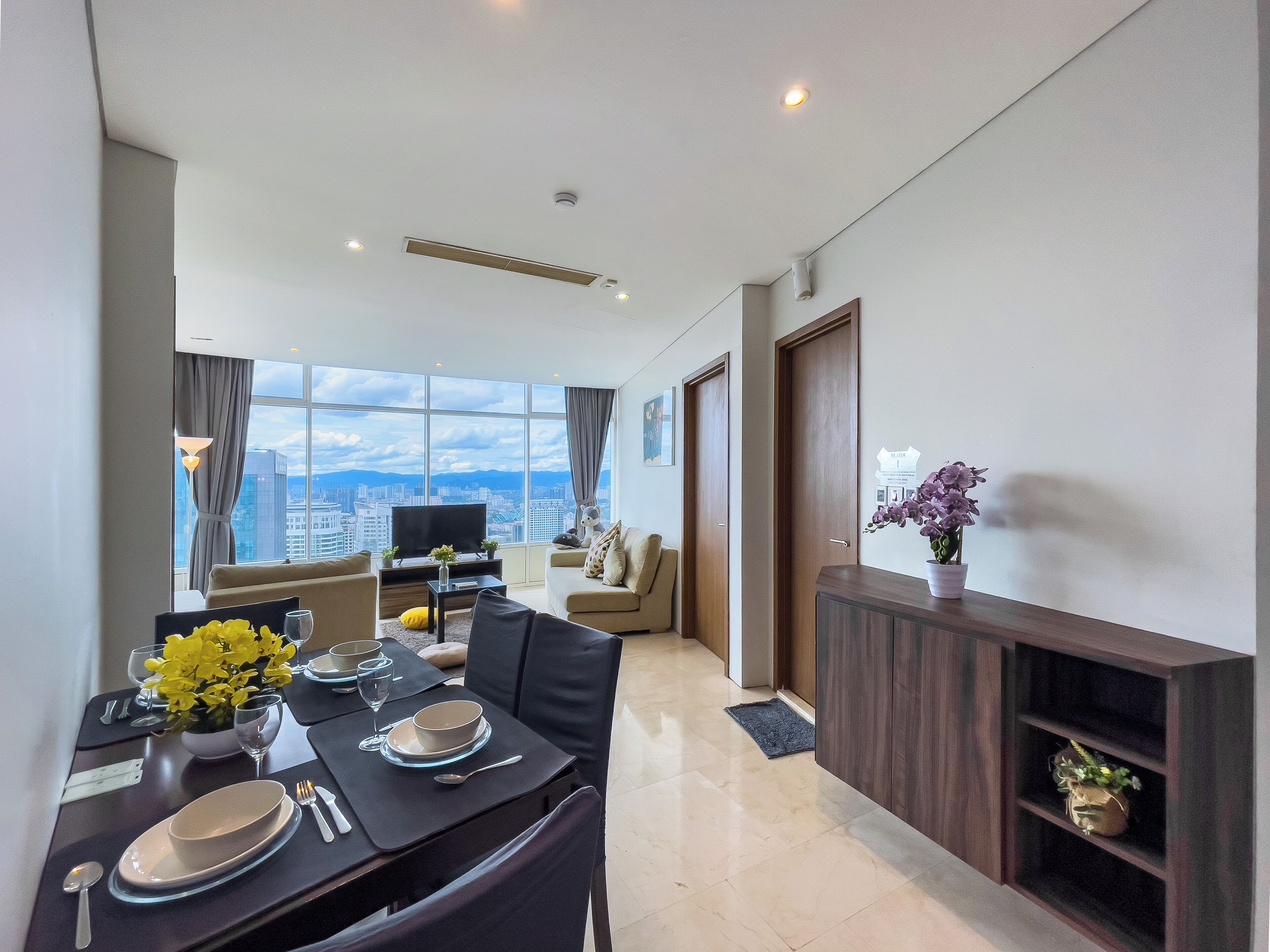 A modern living room with a dining area, large windows, and a view of the cityscape.