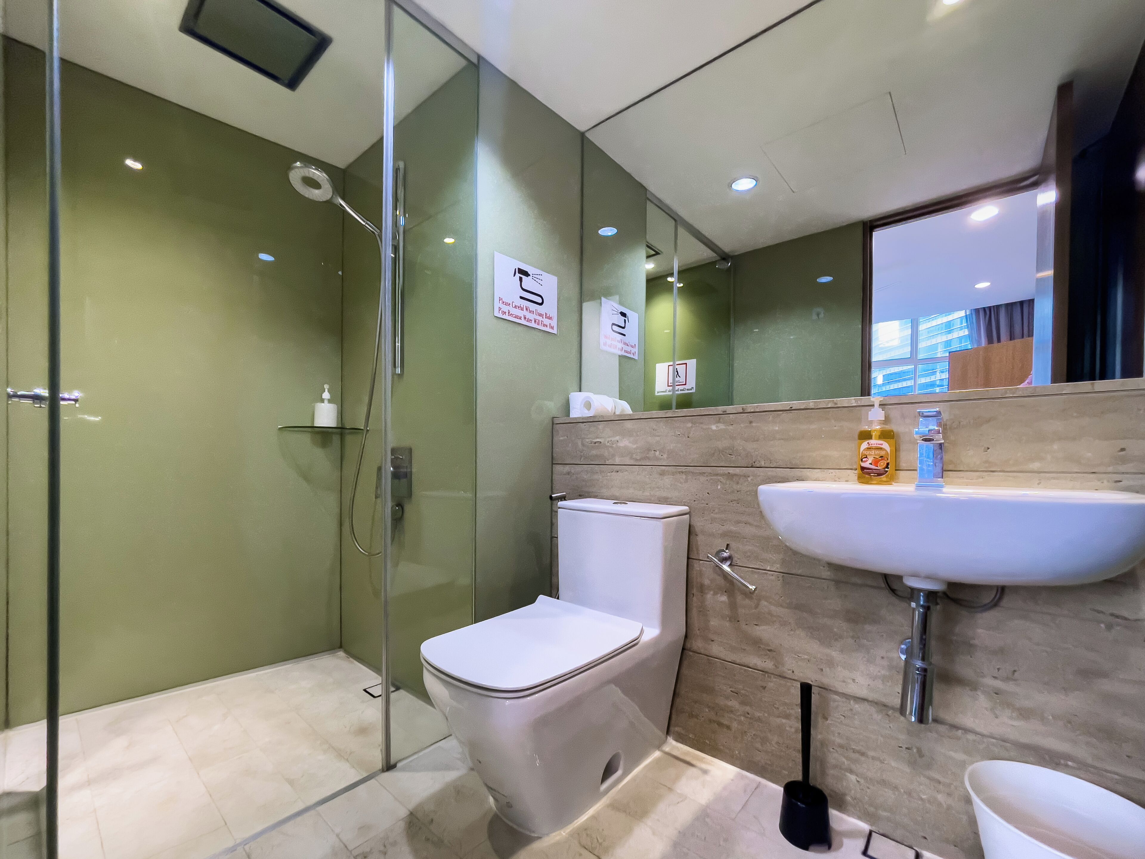 Un baño moderno con cabina de ducha de vidrio, inodoro blanco y lavamanos con dispensadores de jabón.