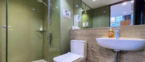 Un baño moderno con cabina de ducha de vidrio, inodoro blanco y lavamanos con dispensadores de jabón.