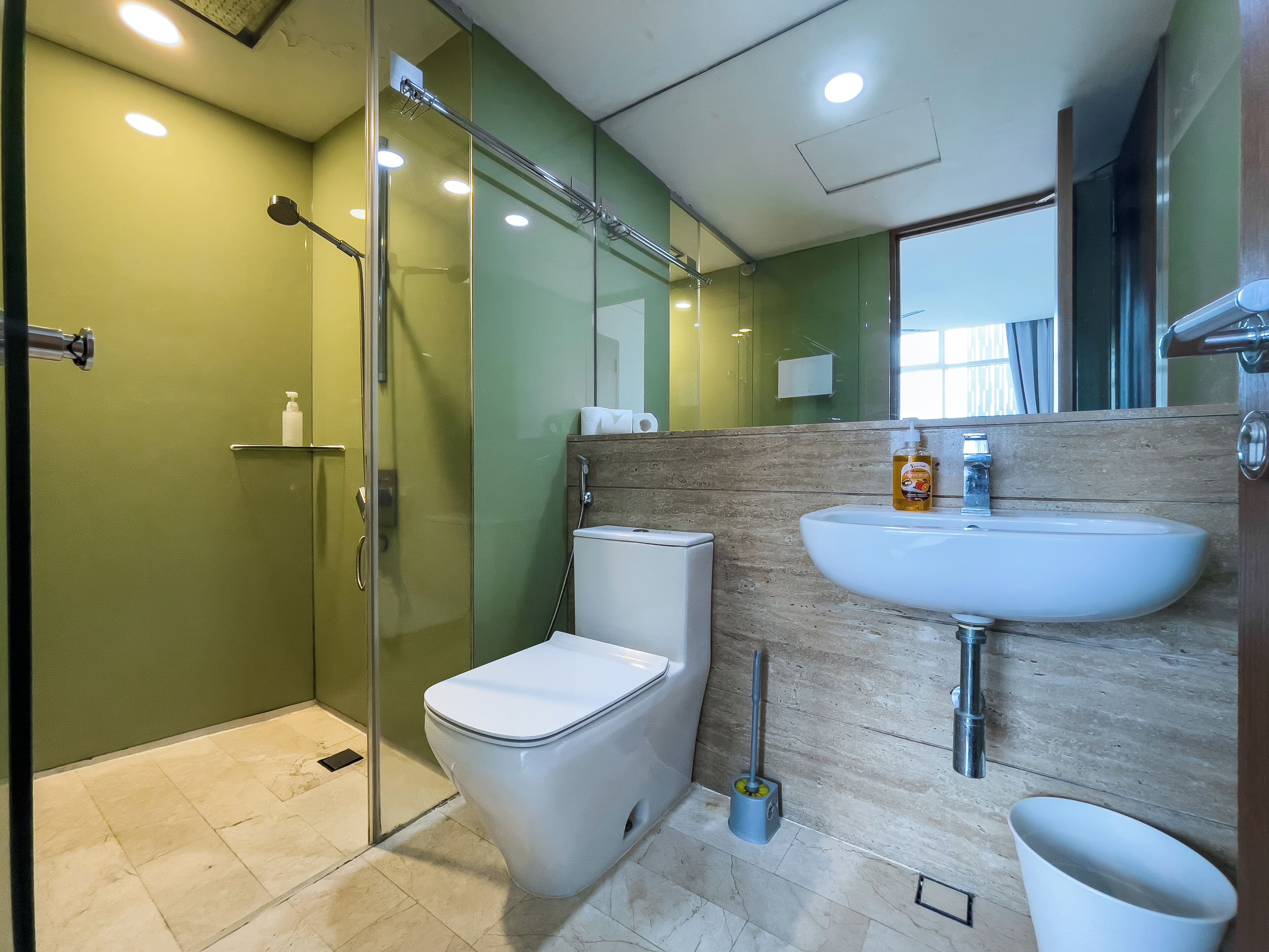 A modern bathroom with a glass shower enclosure, a white toilet, a sink with a wooden backsplash, and a mirror above the sink.
