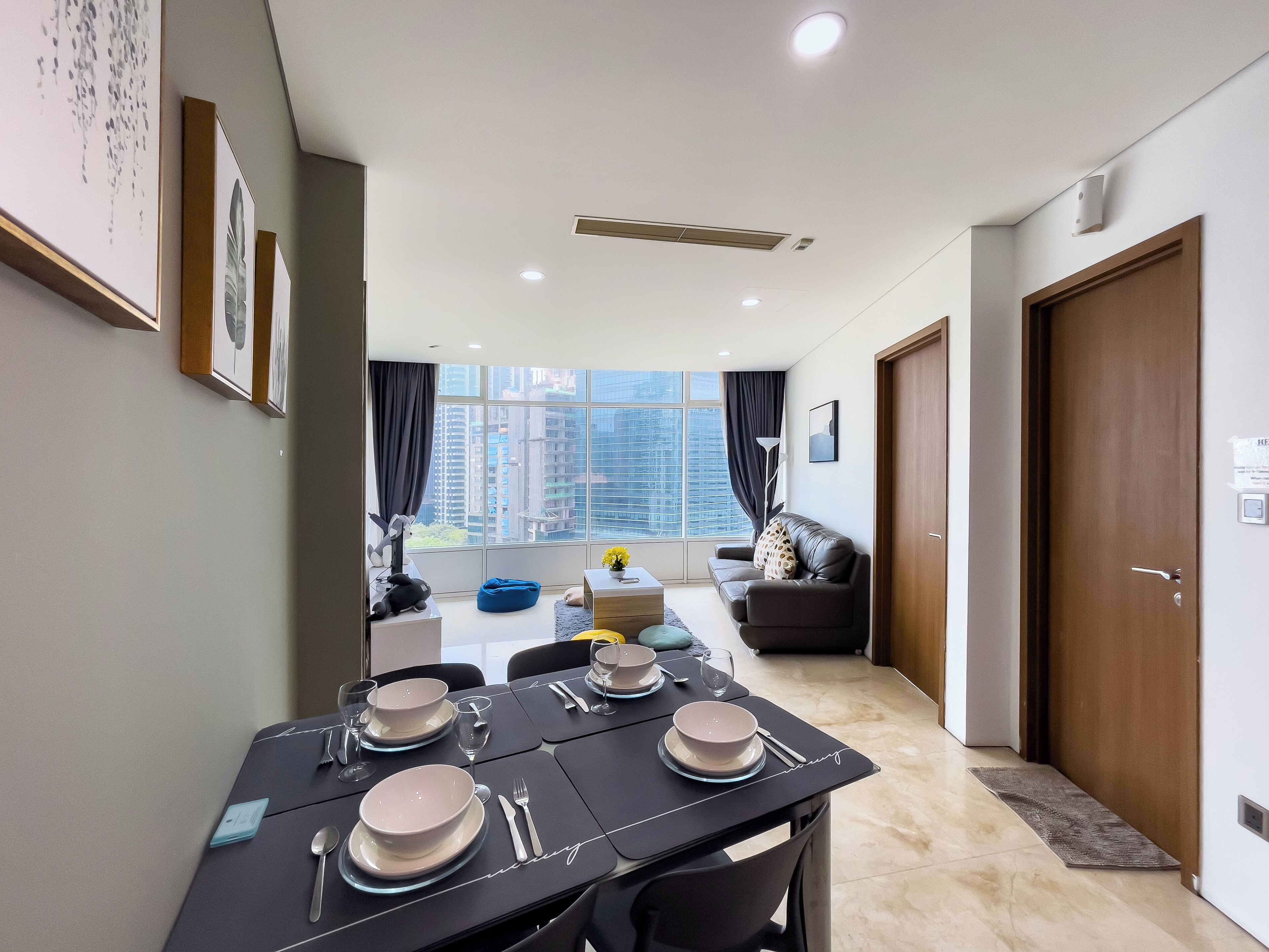A modern dining area with a table set for four, a sofa, and a view of high-rise buildings through large windows.