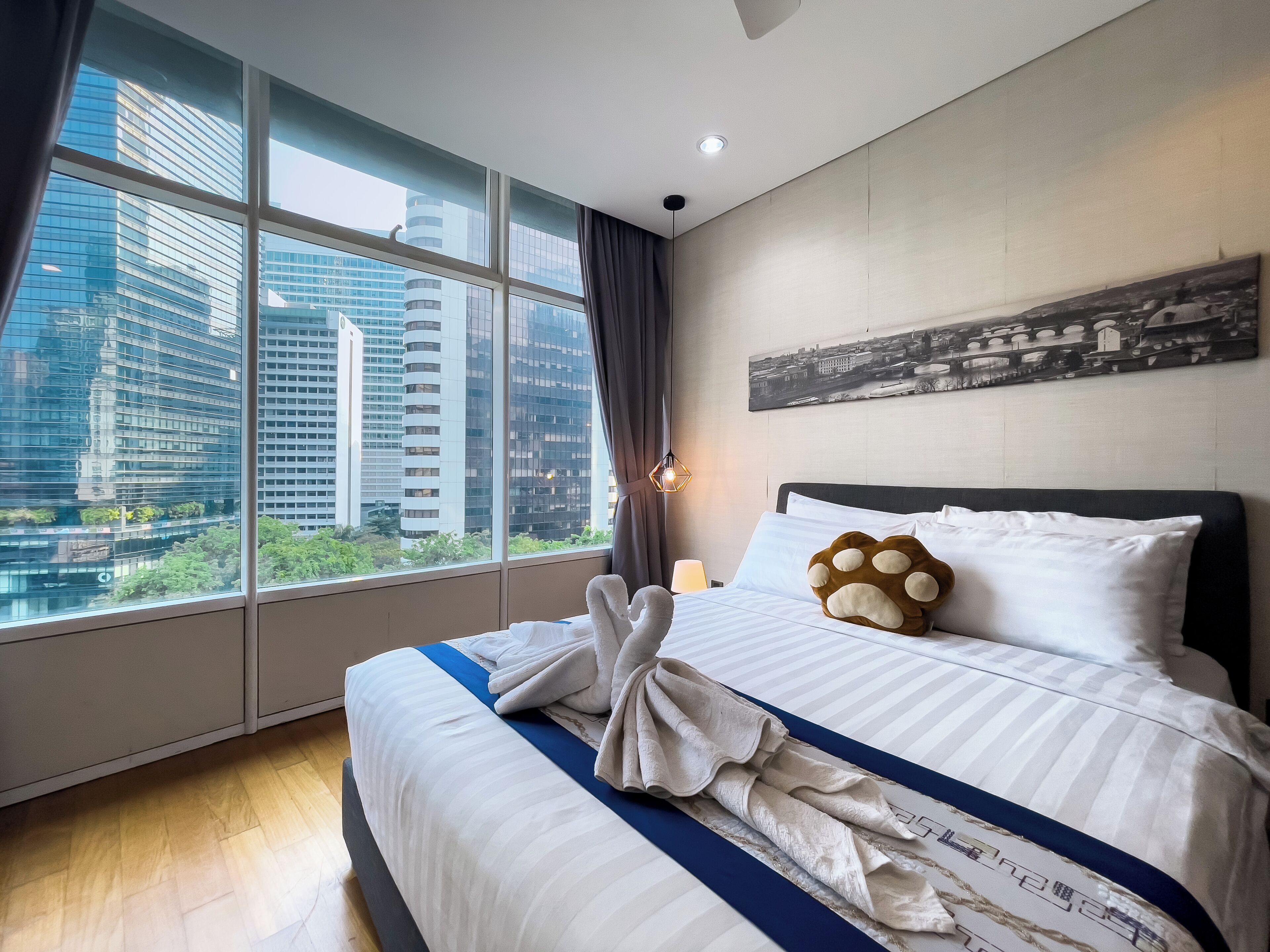 A hotel room with a large window, a bed with white bedding, a blue-striped bedspread, and a cityscape view.