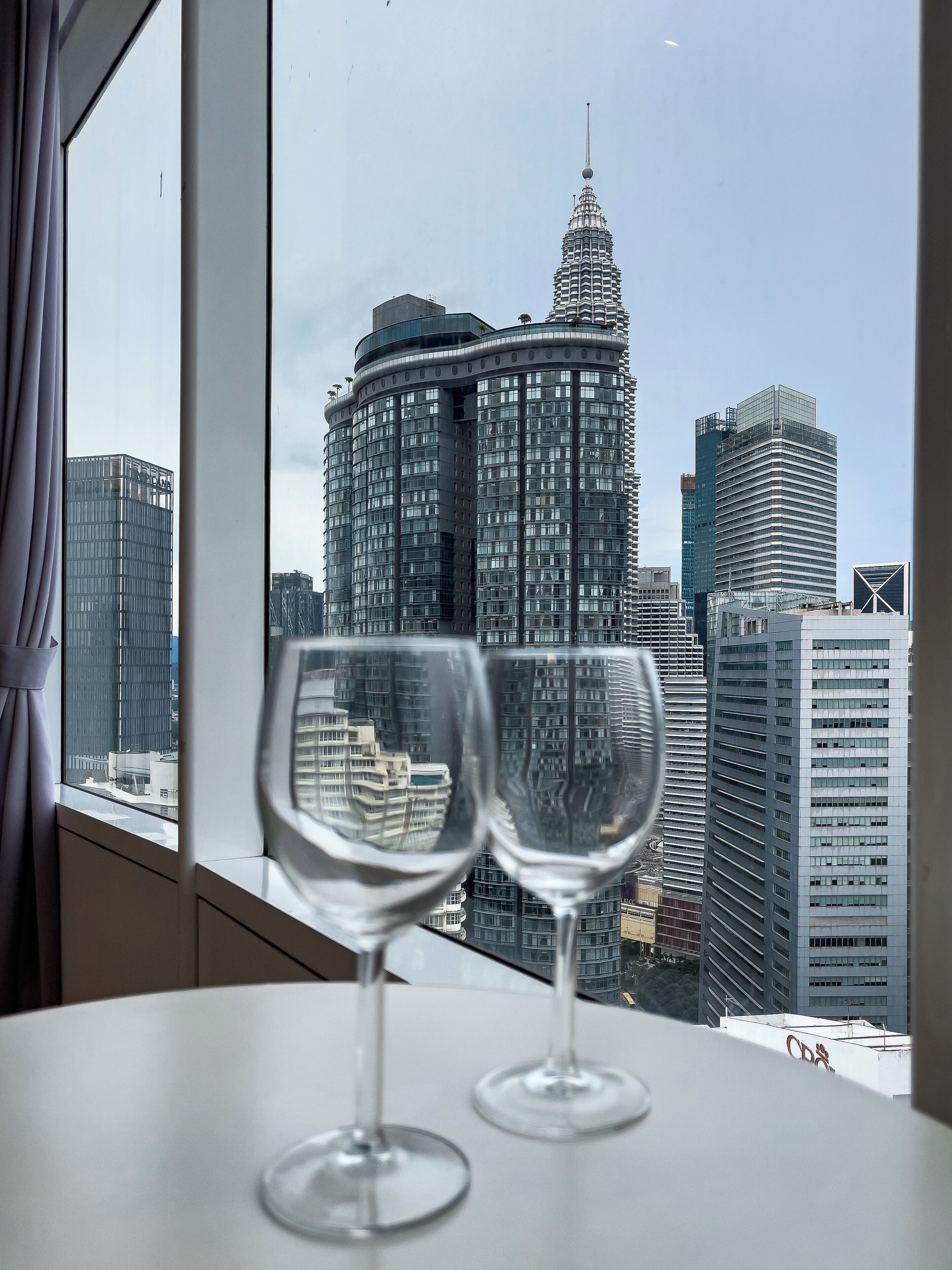 Two empty wine glasses on a table with a view of a city skyline through a window.