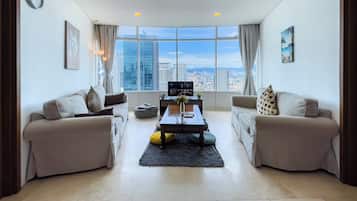 A modern living room with two sofas, a coffee table, and a TV. Large windows offer a city view.