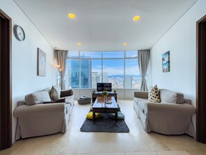 A modern living room with two sofas, a coffee table, and a TV. Large windows offer a city view. - Vortex Suites KLCC By BlackNest (Kuala Lumpur)