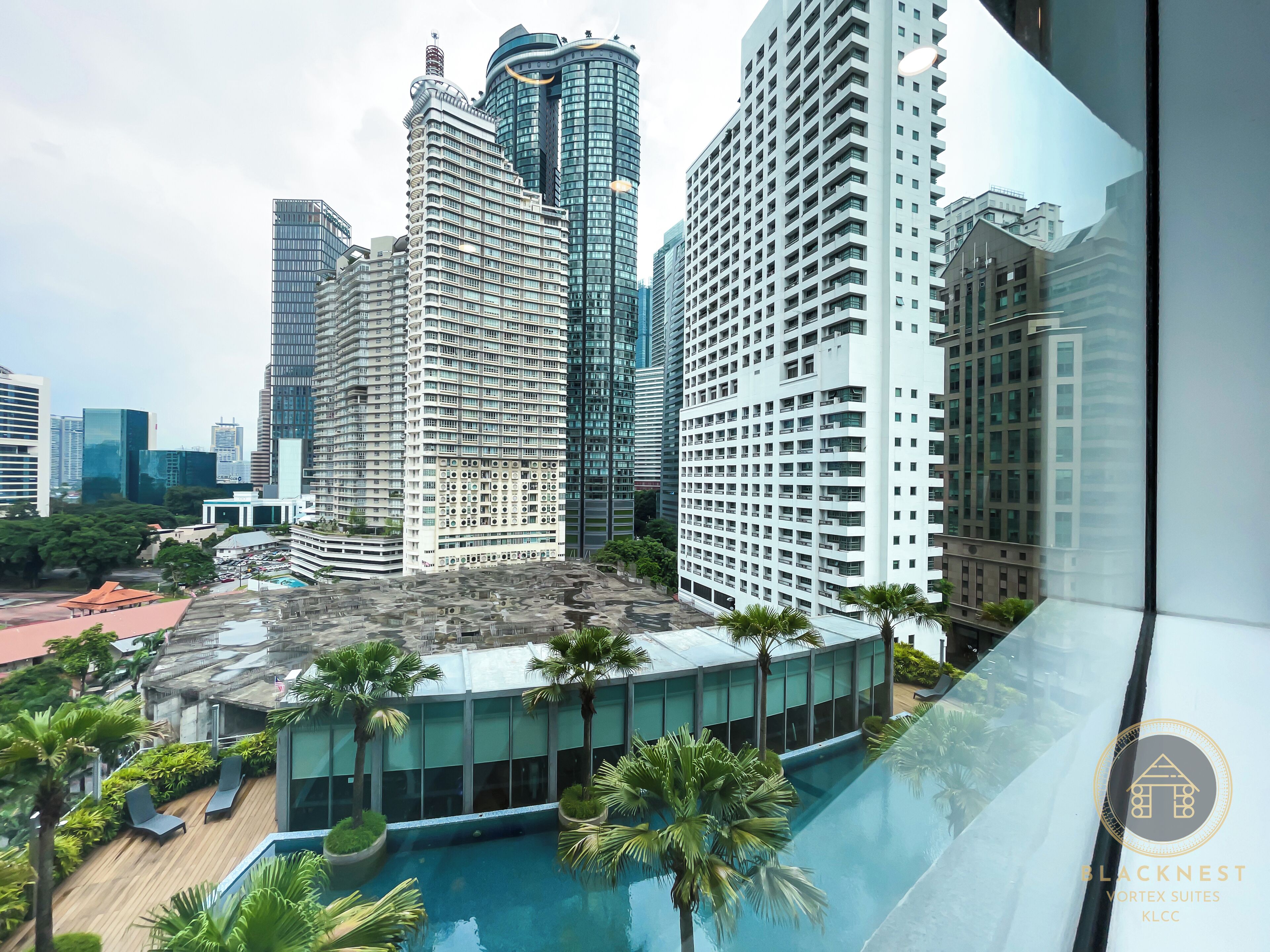 A modern high-rise building with a rooftop pool surrounded by palm trees and lounge chairs.