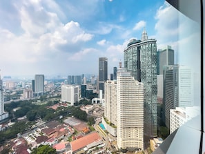 A high-rise building with a distinctive spire, surrounded by other modern skyscrapers and a mix of greenery and urban development. - Vortex Suites KLCC By BlackNest (Kuala Lumpur)