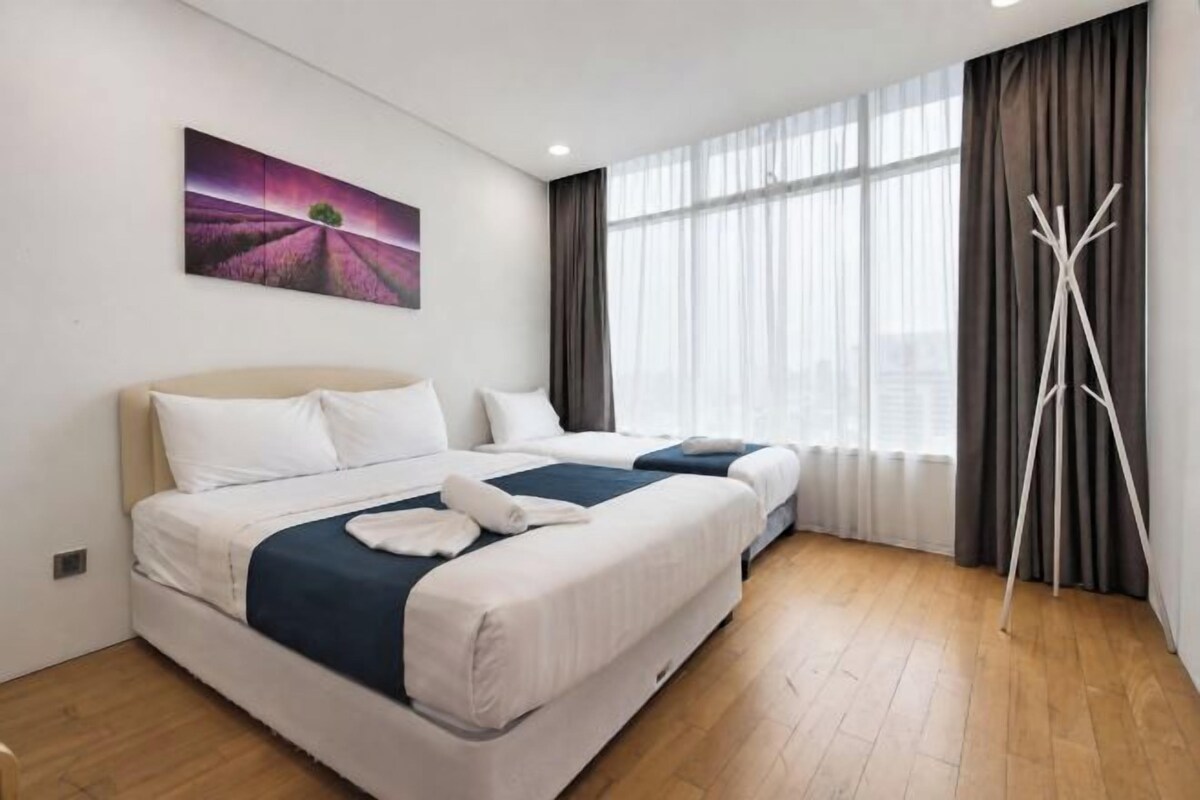 Habitación de hotel con dos camas, un ventanal con cortinas, una lámpara de pie y un cuadro en la pared.
