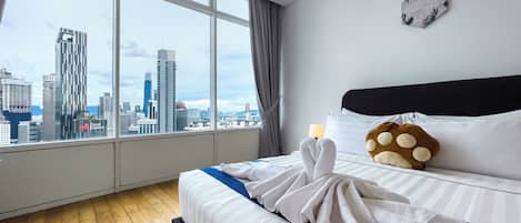A hotel room with a large window, a bed with white linens, a pillow with a paw print design, and a clock on the wall.