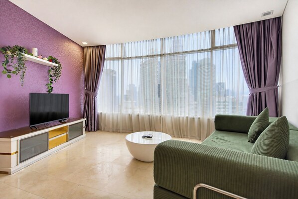 A modern living room with a flat-screen TV, a sofa, a coffee table, and a large window with curtains. - Vortex Suites KLCC By BlackNest (Kuala Lumpur)