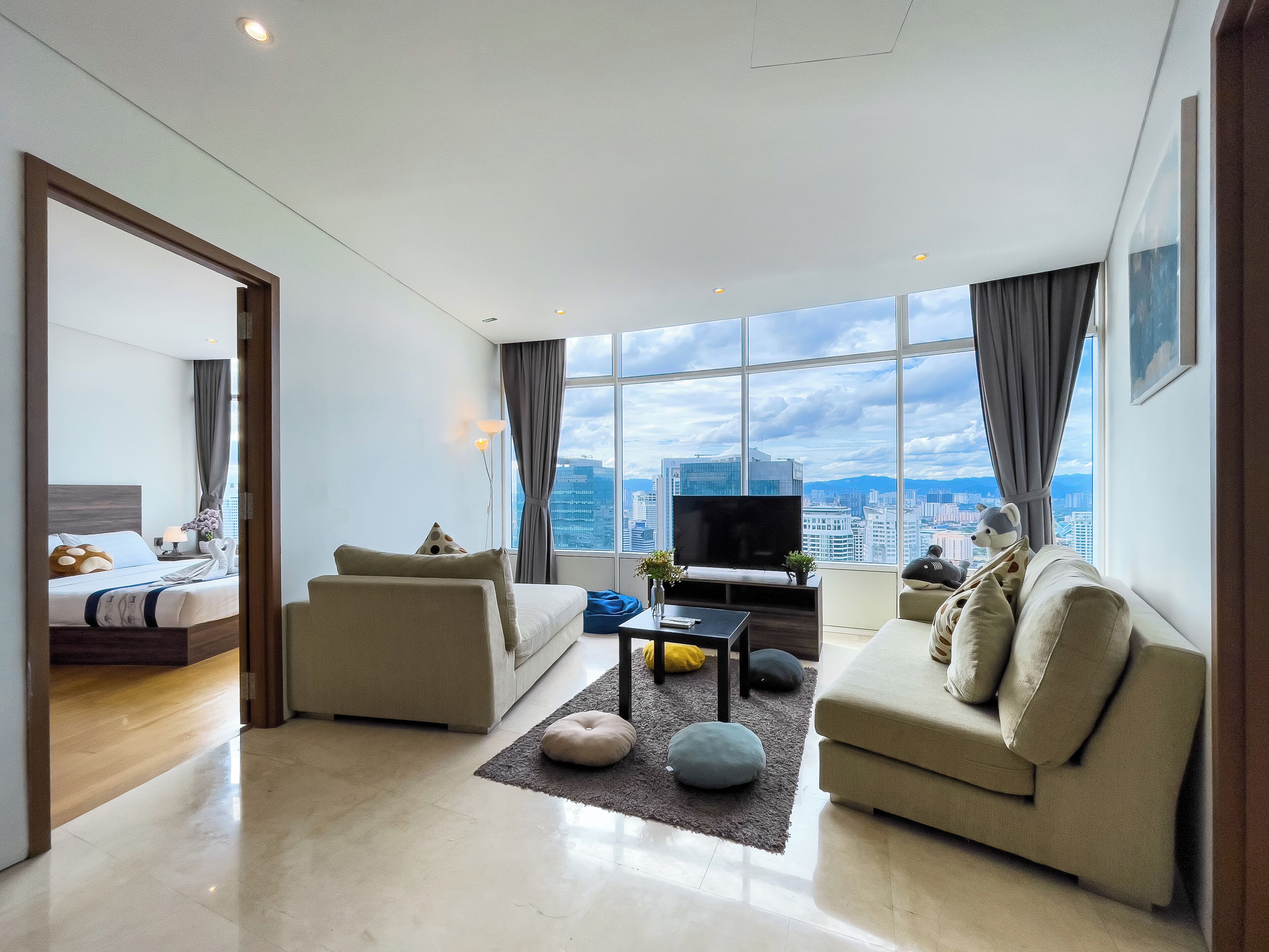 A modern hotel room with a city view, a bed, a sofa, a TV, and a coffee table.