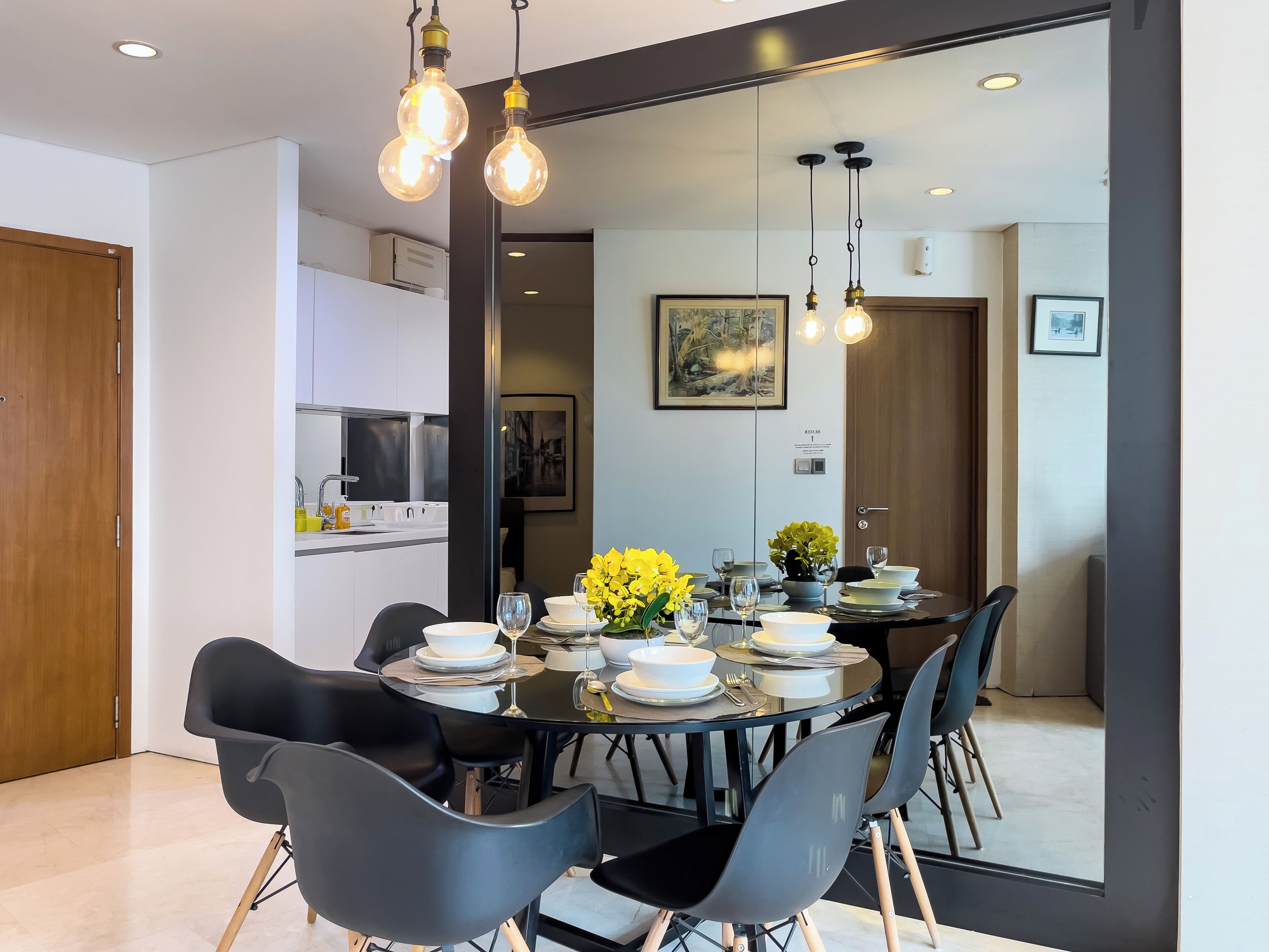 A modern dining area with a round table set for six, black chairs, and a vase of yellow flowers.