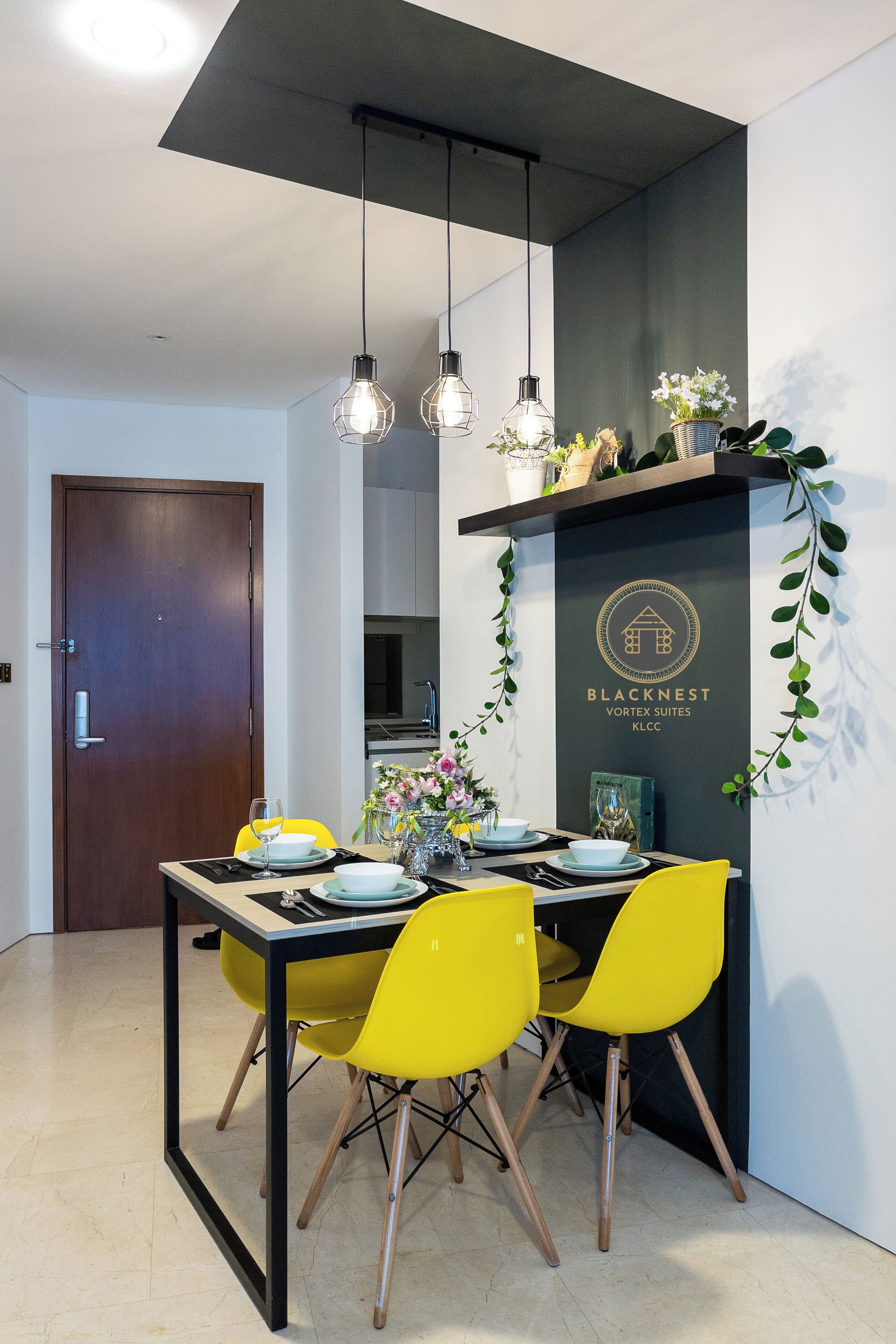A dining area with a black table, yellow chairs, and hanging pendant lights. A sign with the Blacknest logo is visible on the wall.