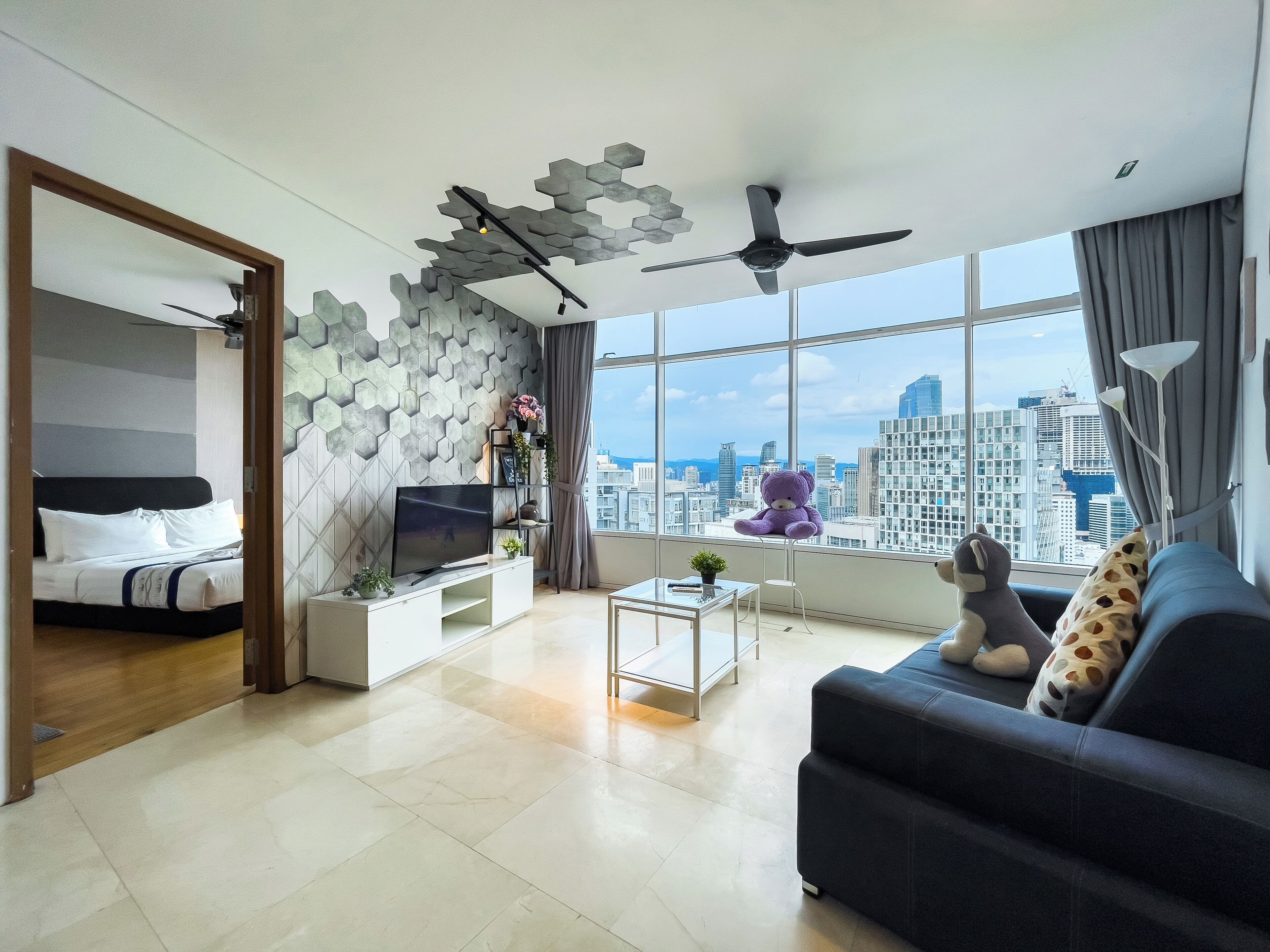 Una sala de estar moderna con cama, televisor, sofá y vistas a la ciudad a través de amplias ventanas.