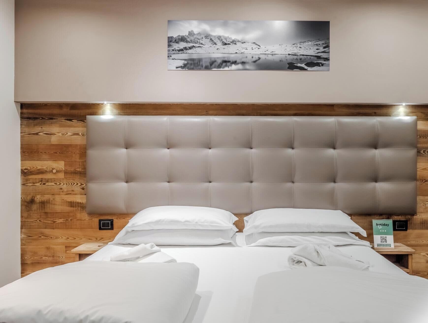 A hotel room with a large bed, wooden headboard, and a framed picture on the wall.