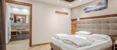 Un dormitorio con techo de madera, una cama con ropa de cama blanca, cabecera de madera y un baño con espejo y lavamanos.