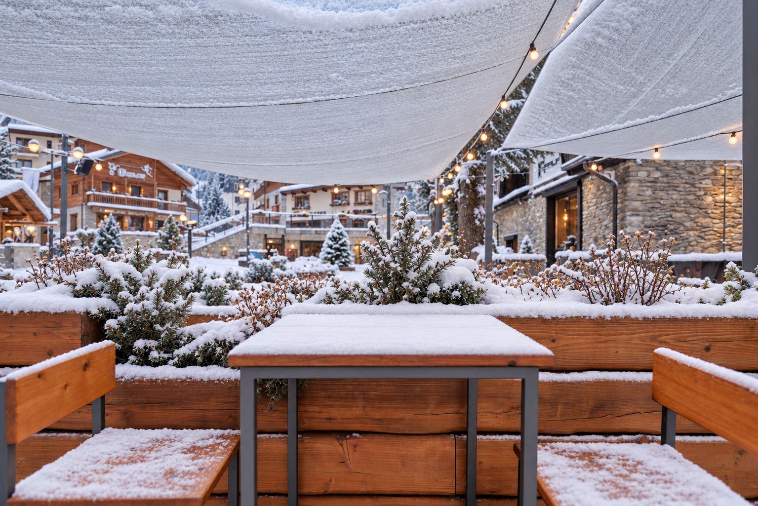 A snow-covered outdoor seating area with wooden benches and tables, surrounded by snow-laden plants and trees, under a canopy.