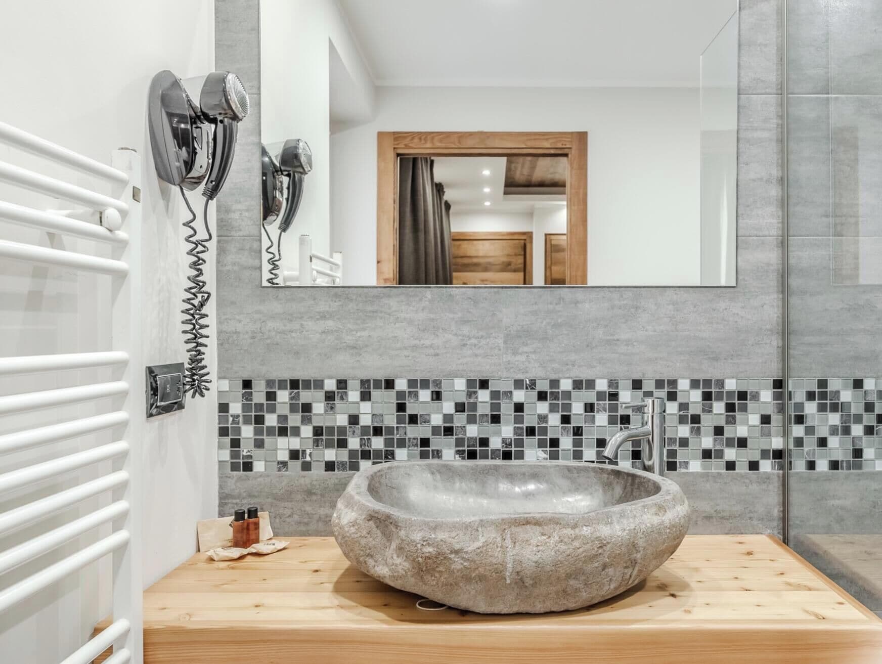 A bathroom with a stone sink, a mirror, and a hairdryer mounted on the wall.