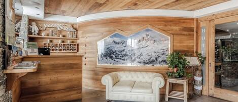 A reception area with a wooden ceiling, a large framed mountain landscape, a white sofa, and a reception desk with various items.