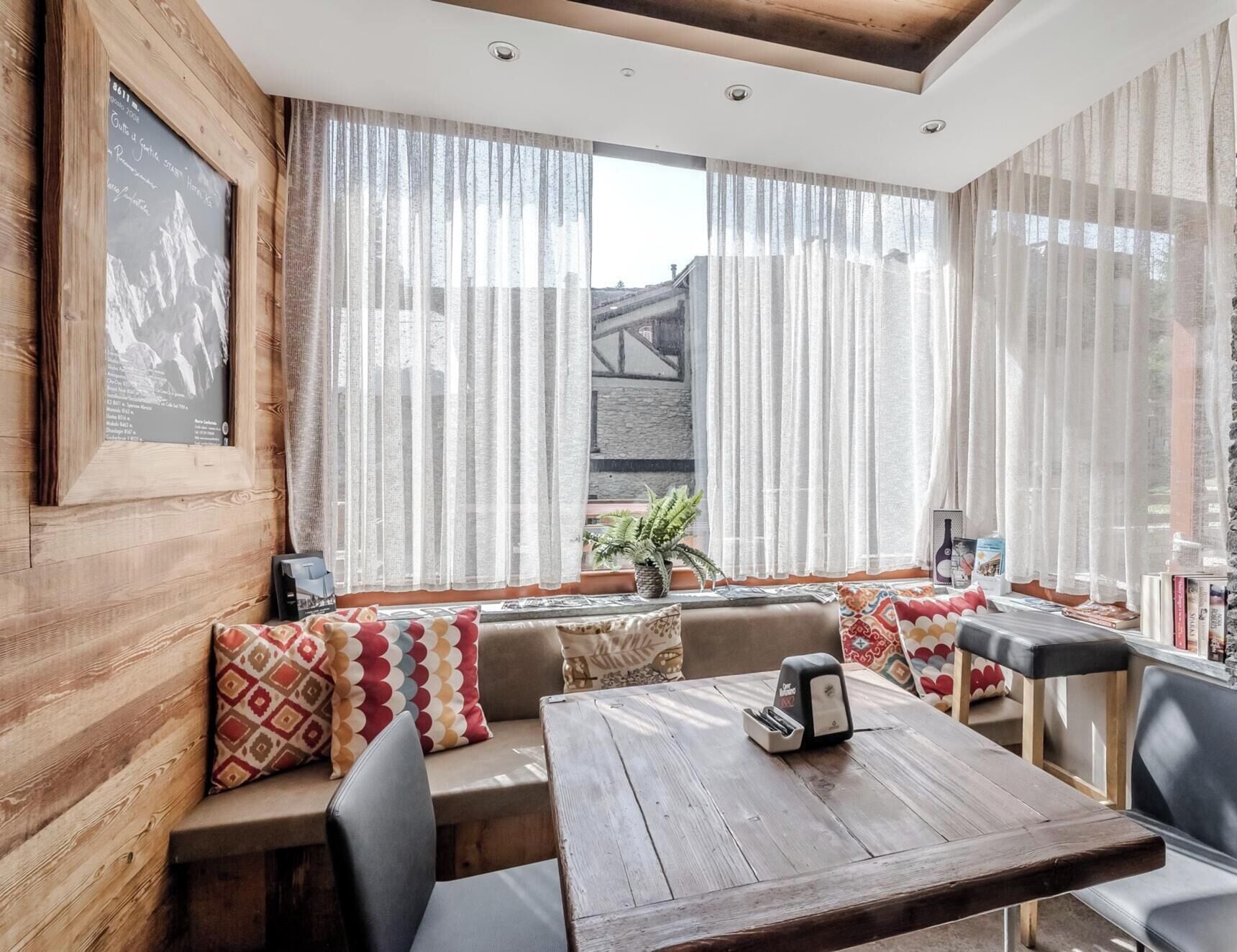 A cozy seating area with a wooden table and chairs, a framed picture on the wall, and sheer curtains.
