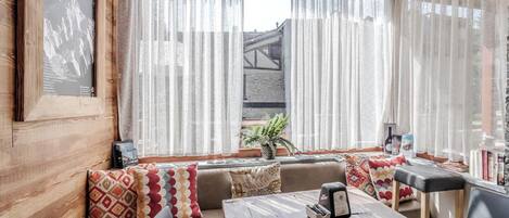 A cozy seating area with a wooden table and chairs, a framed picture on the wall, and sheer curtains.