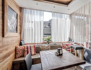 A cozy seating area with a wooden table and chairs, a framed picture on the wall, and sheer curtains.