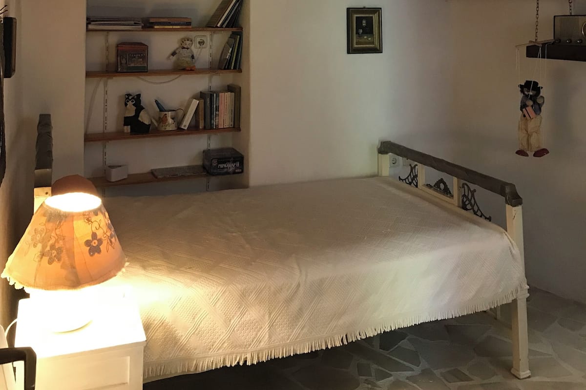 A cozy room with a bunk bed, a bedside lamp, a shelf with books and decorative items, and a hanging light fixture.