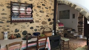 A rustic dining area with a stone wall, a wooden table with a striped tablecloth, and a black stove.