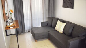 Uma sala de estar moderna com um sofá modular cinzento, uma mesa de apoio de madeira com um vaso e controles remotos, um espelho grande e uma obra de arte na parede.