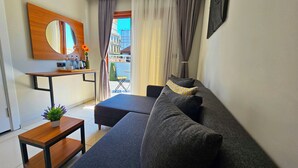Uma sala de estar moderna com um sofá cinzento, uma pequena mesa de madeira e um espelho grande.