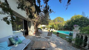 An outdoor patio with a sofa, chairs, and a table. There is a pool in the background.