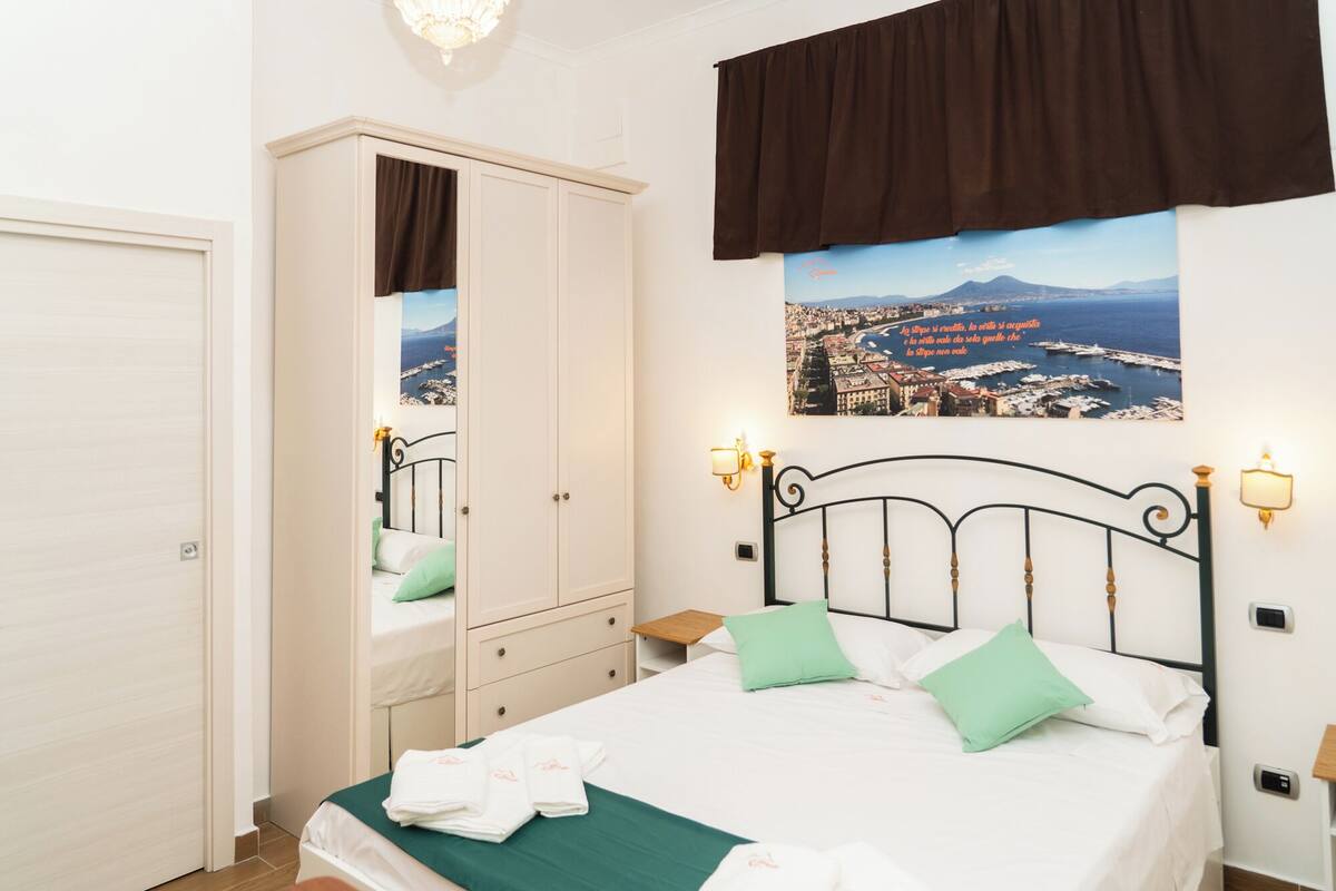 A bedroom with a bed, a wardrobe, a nightstand, and a wall-mounted lamp.