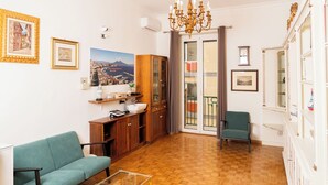 A living room with a sofa, a wooden cabinet, a chandelier, and a view of a balcony. - Suite Cervantes (Naples)