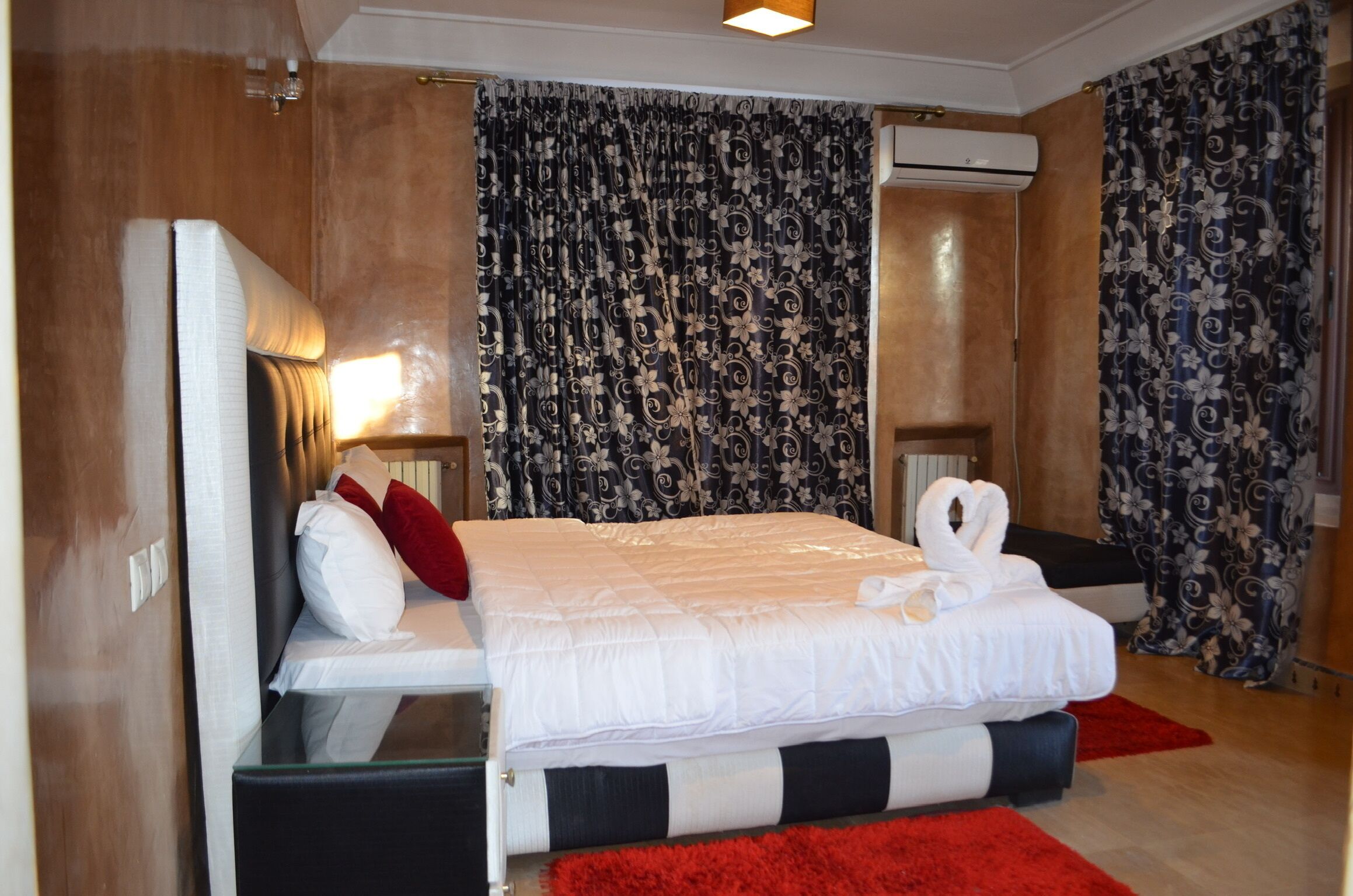 Et moderne hotelværelse med en stor seng, et sengebord, et spejl og en rød måtte.