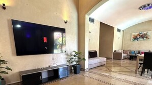 A spacious living area with a flat-screen TV mounted on the wall, a sofa, a coffee table, and a dining area with chairs. - Villa in the heart of Marrakech (Bab Ighl Marrakesh,)