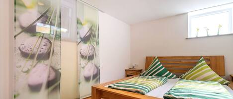 A bedroom with a wooden bed, green and white striped pillows, a wooden nightstand, and a window with flowers.