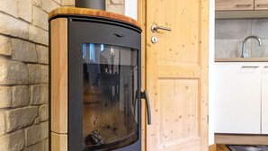 Een houtkachel in een keuken met een stenen muur, houten kasten en een houten deur.