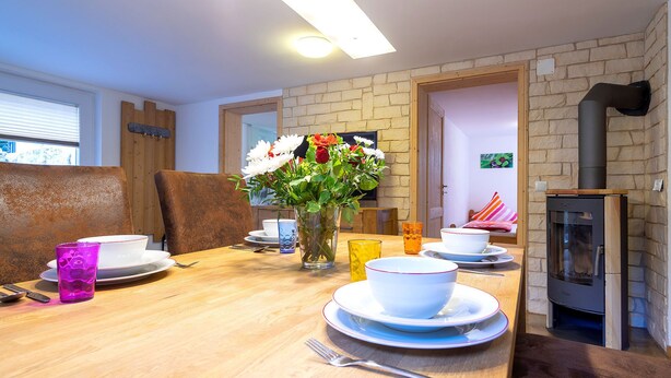 Een eethoek met een houten tafel gedekt voor twee personen, een bloevas en een open haard.