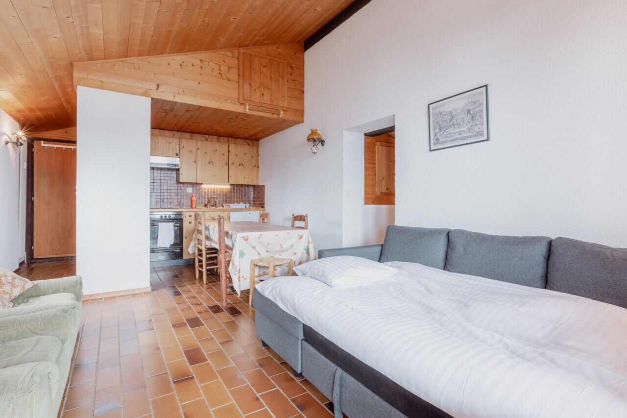 A cozy room with a bed, a sofa, a dining table with chairs, and a kitchen area.