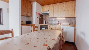 A compact kitchen with wooden cabinets, a dining table with a fruit-patterned tablecloth, and a small dishwasher.