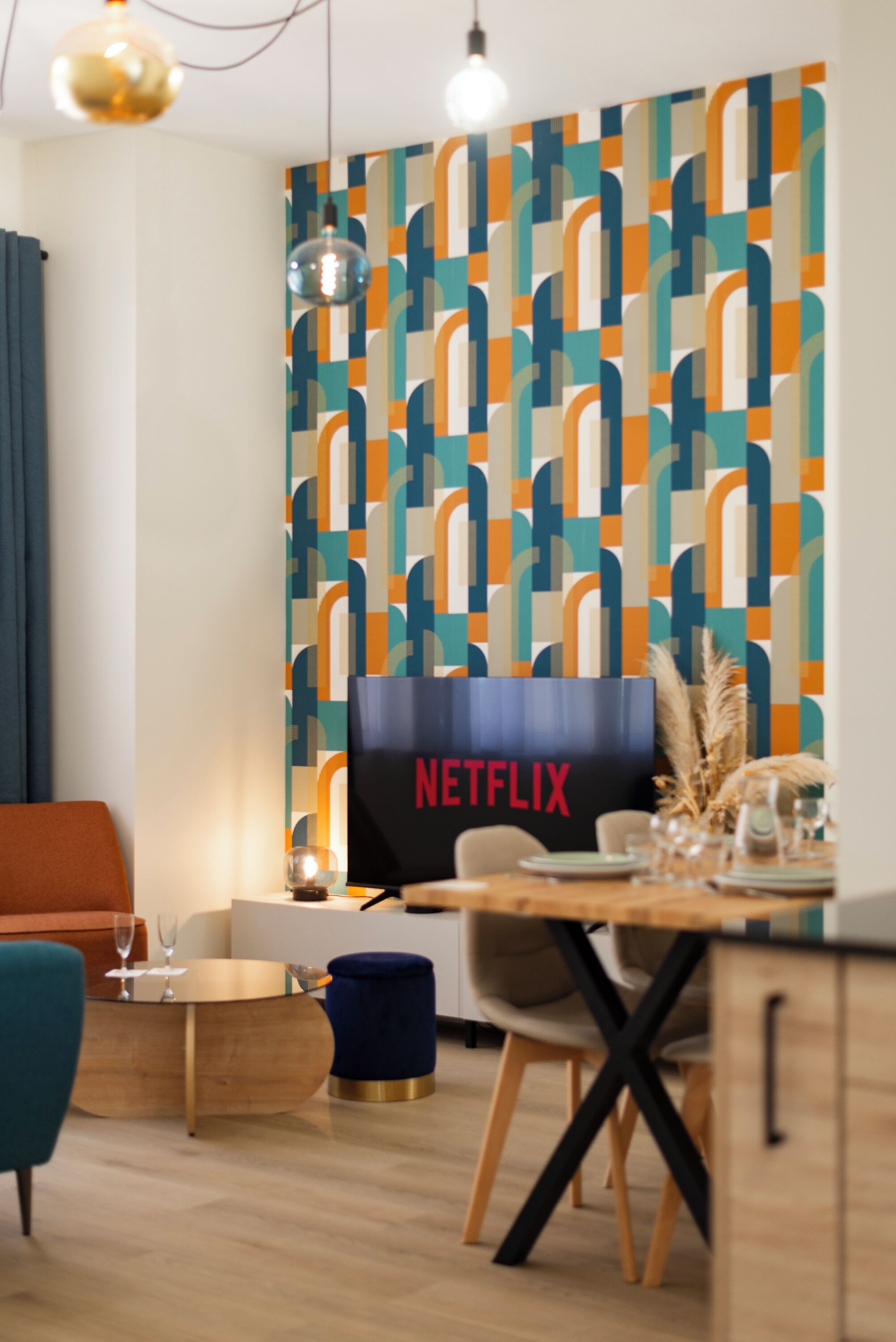 Ein moderner Essbereich mit Wand in geometrischem Muster, einem Netflix-Schild, einem Holztisch und einem blauen Pouf.