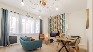 A modern living room with a sofa, dining table, chairs, a TV, and a patterned wall. - F3 au Coeur des Cordiers, Avec Parking Privatif Inclus (Le Tréport)