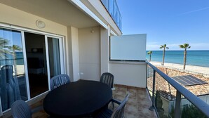Ein Balkon mit Tisch und Stühlen, eine Schiebetür, eine Whiteboard-Tafel und Blick auf Strand und Meer.