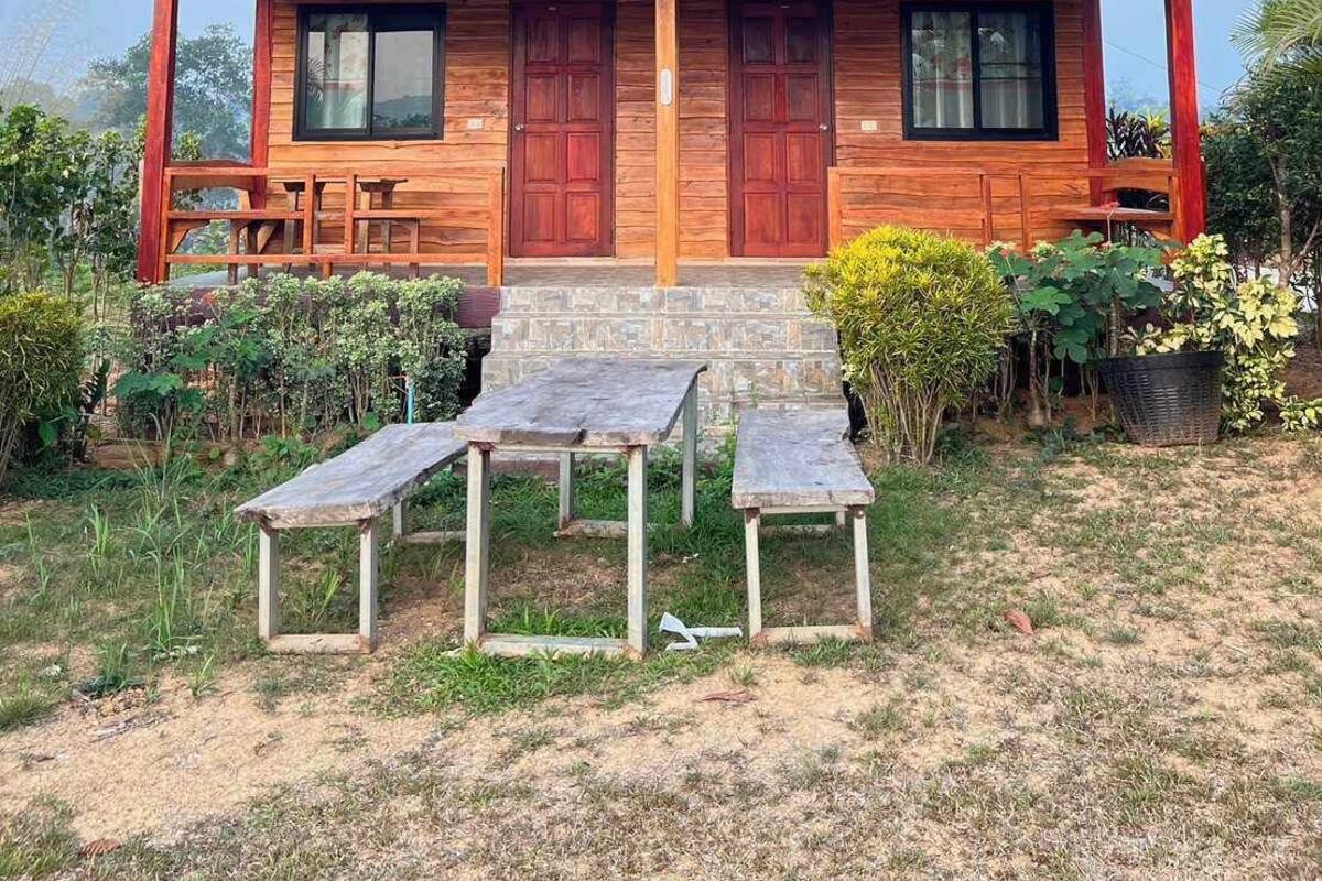 Une cabane en bois avec une véranda, deux portes et un petit espace extérieur aménagé pour s’asseoir.